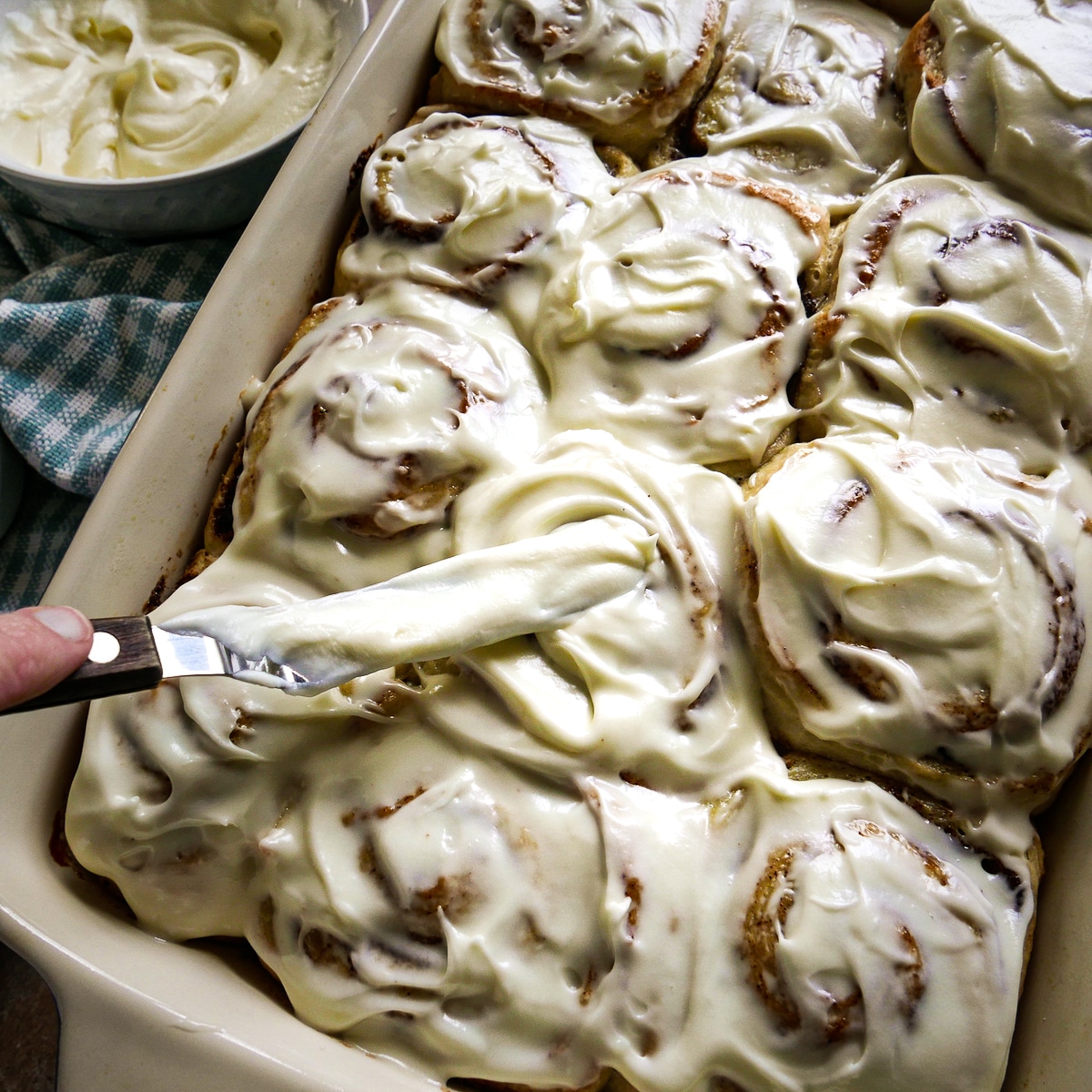 Spreading cream cheese frosting over cooled cinnamon rolls.