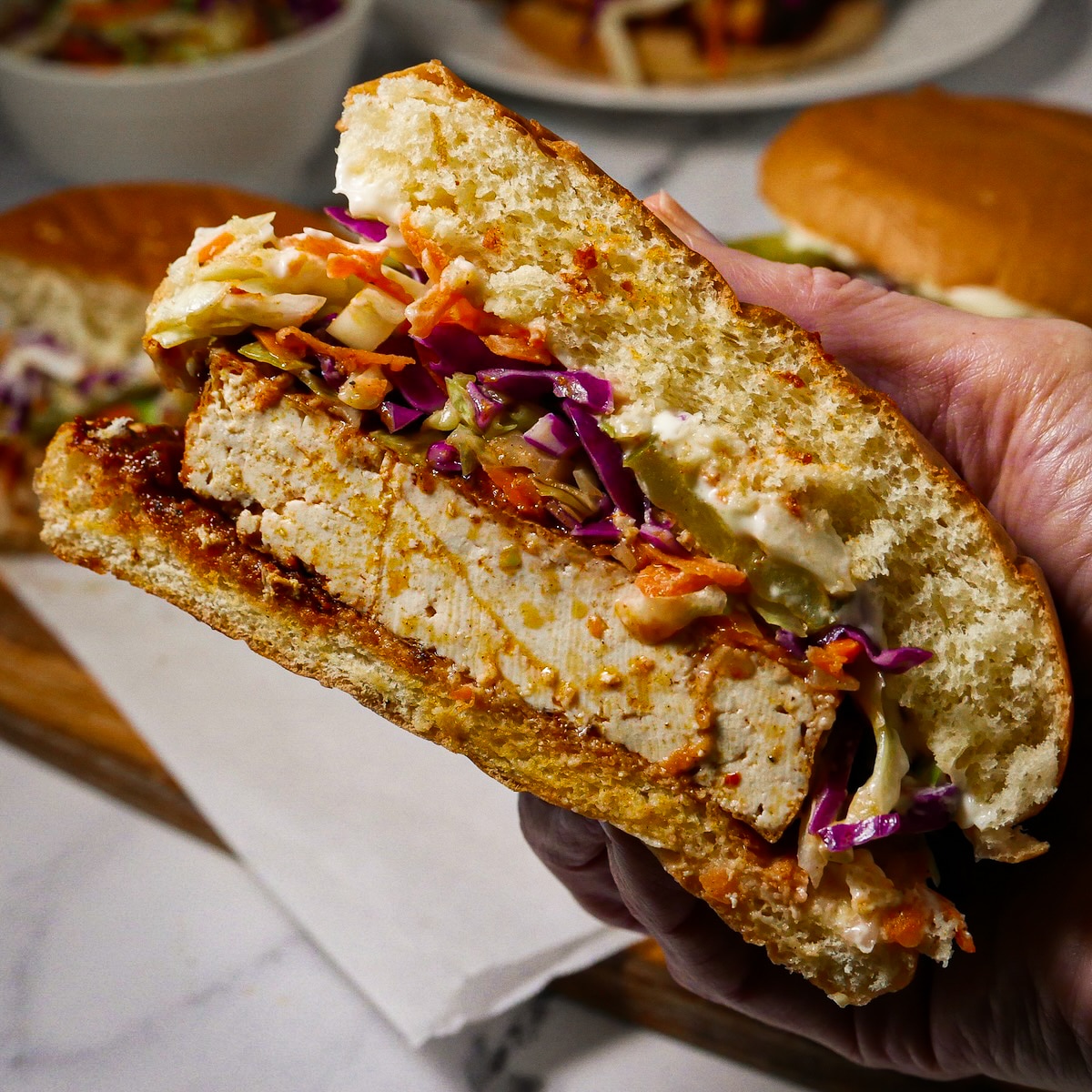 crispy-tofu-sandwich.jpg Holding a crispy tofu sandwich.