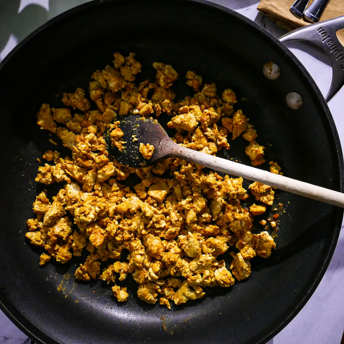Scrambled tofu coated with sauce in a skillet. 