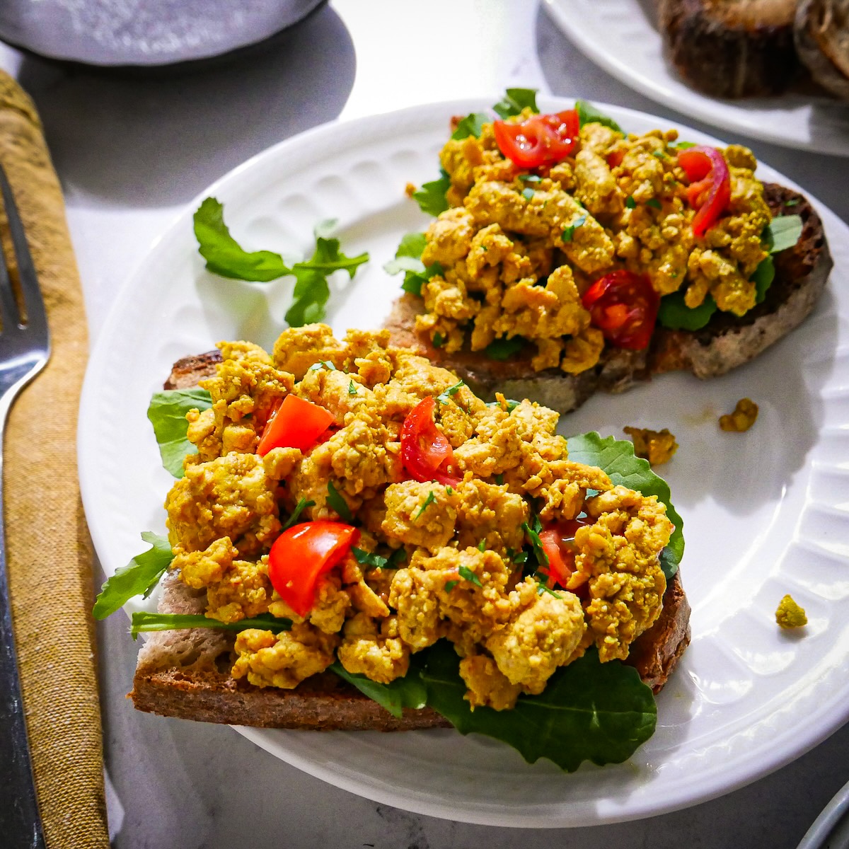 Two pieces of scrambled tofu toast with cherry tomatoes and arugula. 