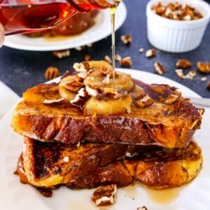Rich french toast with caramelized bananas and syrup being poured on top.