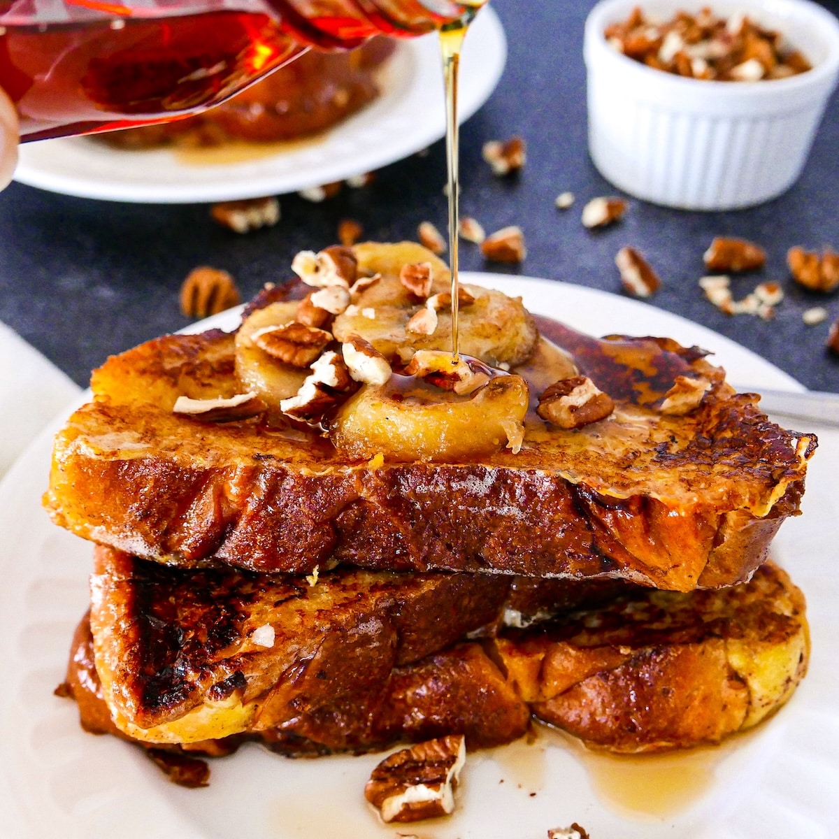 french-toast-with-caramelized-bananas-and-maple-syrup.jpg Rich french toast with caramelized bananas and syrup being poured on top.