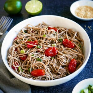 Spicy miso noodles with roasted tomatoes in a white bowl with two forks.