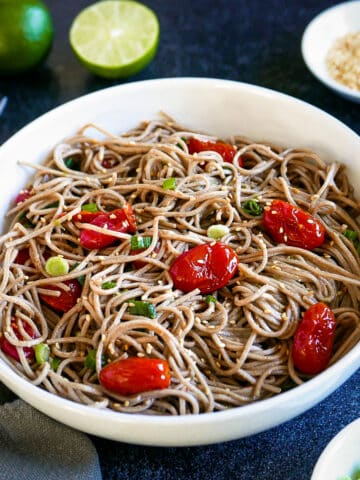 Spicy miso noodles with roasted tomatoes in a white bowl with two forks.