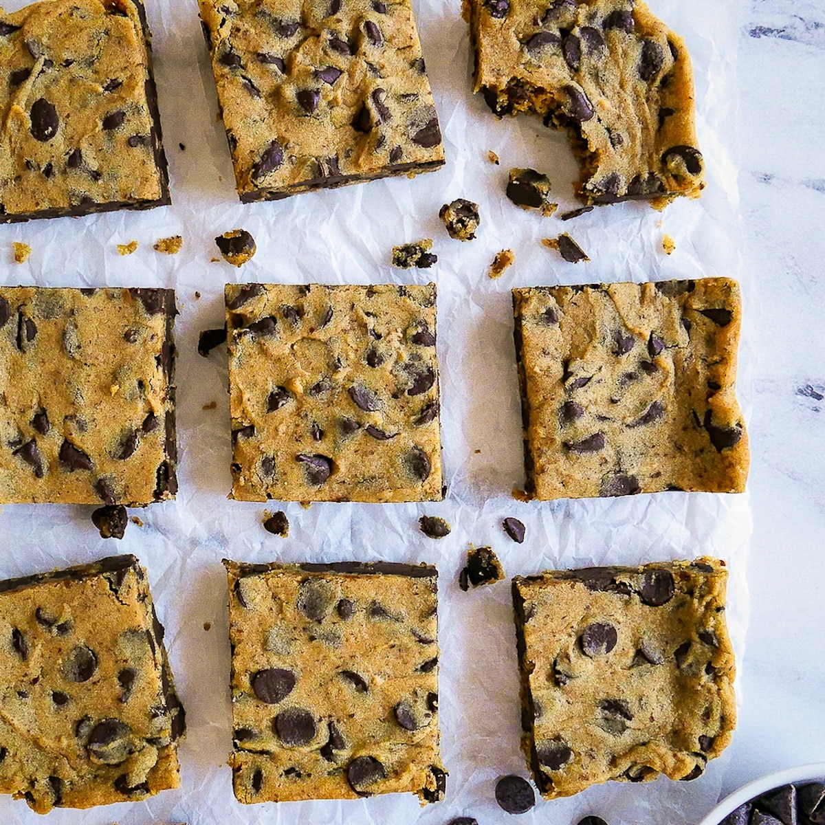 healthy-blondies.jpg Healthy blondies arranged on parchment paper and cut into squares with one missing a bite.