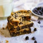 Vegan blondies stacked on parchment paper with chocolate chips in background.
