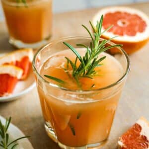 grapefruit cocktail in a glass garnished with rosemary and slice of grapefruit.