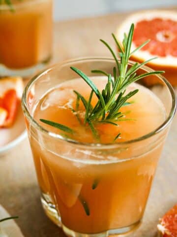 grapefruit cocktail in a glass garnished with rosemary and slice of grapefruit.