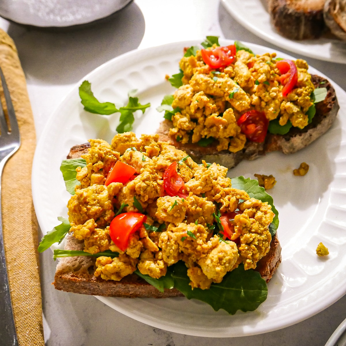 Two pieces of scrambled tofu toast with cherry tomatoes and arugula.