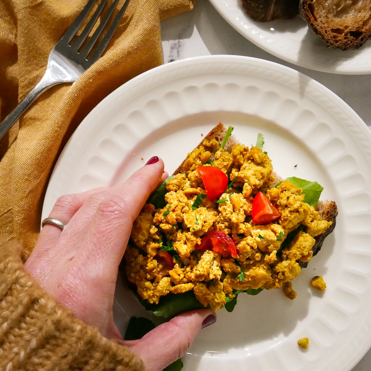 Hand picking up piece of tofu egg scramble on toast.
