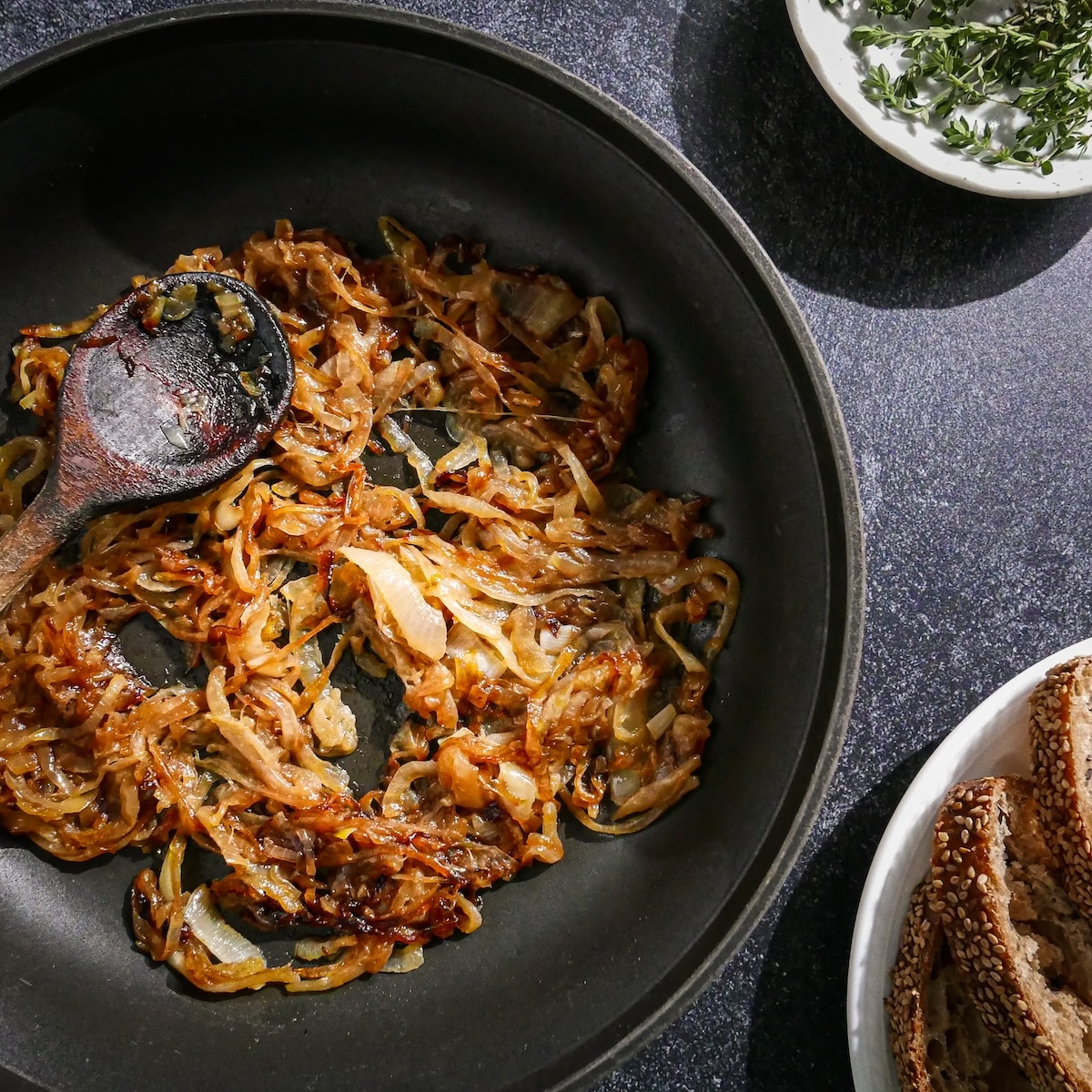 Sliced onion being caramelized in a skillet with a wooden spoon.
