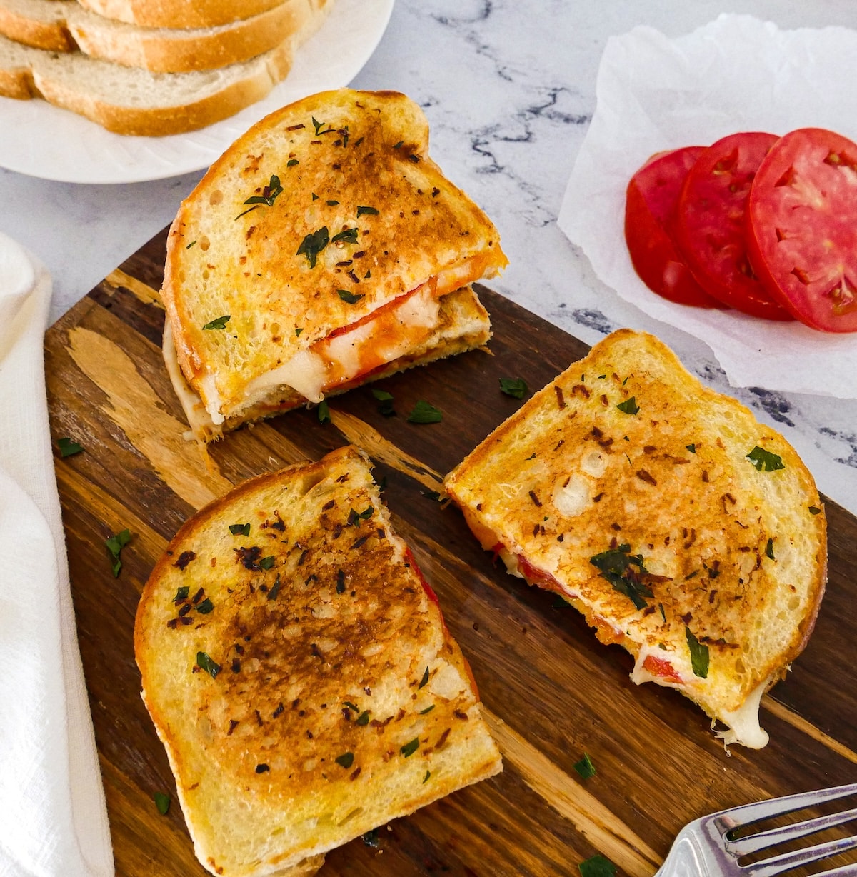 melty-grilled-cheese.jpg Three pieces of melty grilled cheese on cutting board with tomato and sourdough slices.