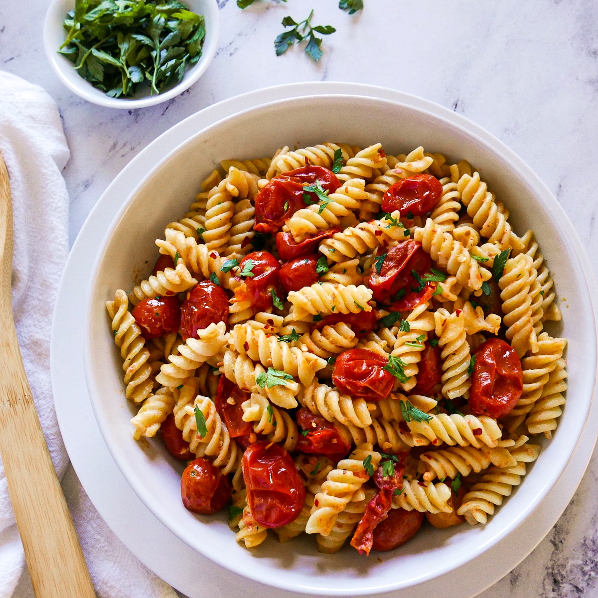 bowl of vegan tahini pasta and cherry tomatoes resting on a plate.