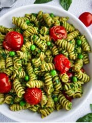 Creamy pea pesto pasta with roasted tomatoes in a white bowl.