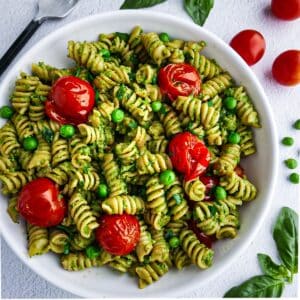 Creamy pea pesto pasta with roasted tomatoes in a white bowl.