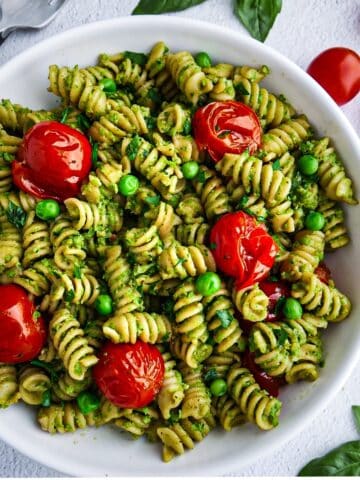 Creamy pea pesto pasta with roasted tomatoes in a white bowl.
