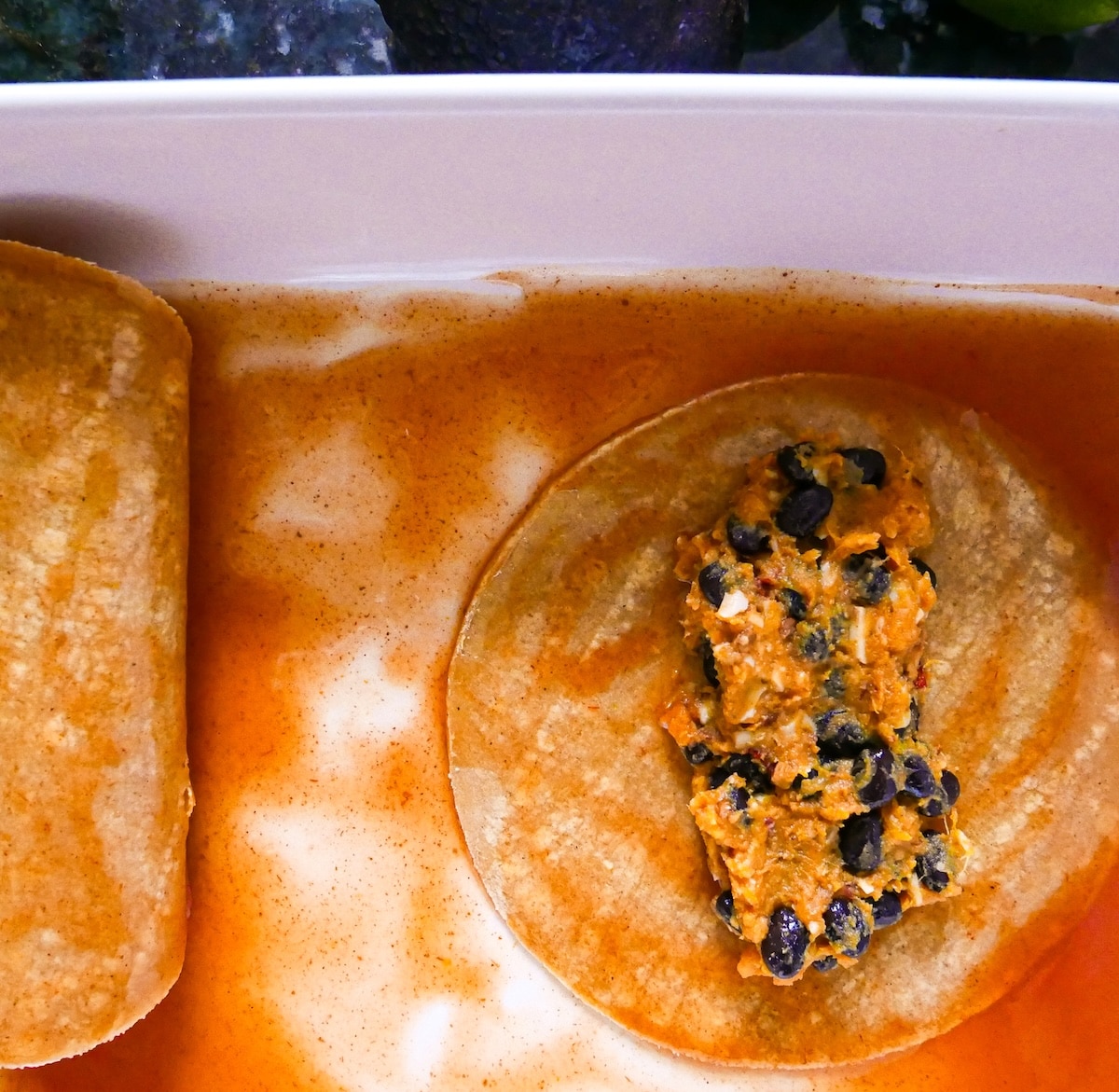 assembling-enchiladas.jpg Corn tortilla coated in enchilada sauce, with filling placed down the middle.