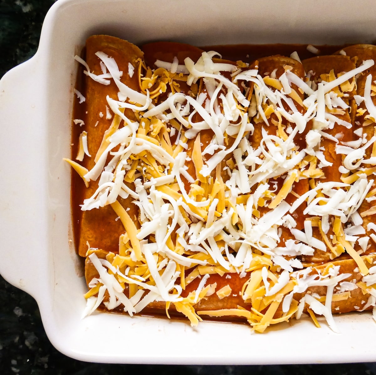 assembled-sweet-potato-enchiladas.jpg Assembled sweet potato enchiladas topped with red enchilada sauce and cheese.