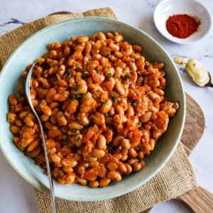 Bowl of vegetarian baked beans resting on a cutting board with a spoon.