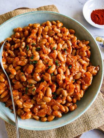 Bowl of vegetarian baked beans resting on a cutting board with a spoon.