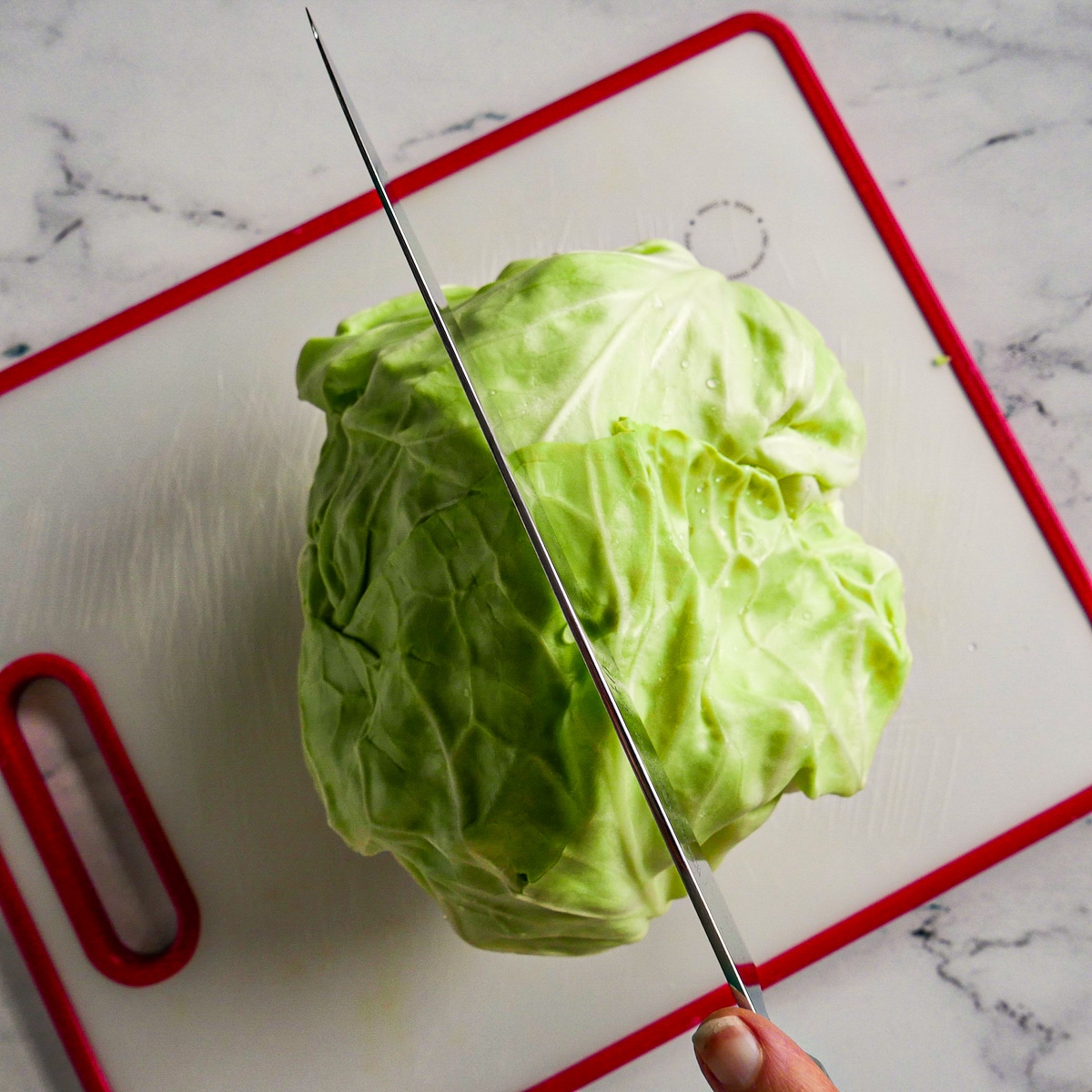 slicing-cabbage-in-half.jpg Knife slicing a green cabbage in half on a cutting board.