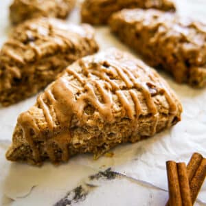 Flaky cinnamon scones with a glaze arranged on parchment paper.