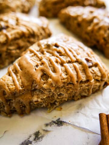 Flaky cinnamon scones with a glaze arranged on parchment paper.