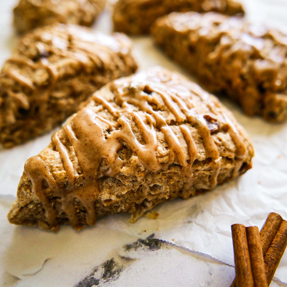 Flaky cinnamon scones with a glaze arranged on parchment paper.