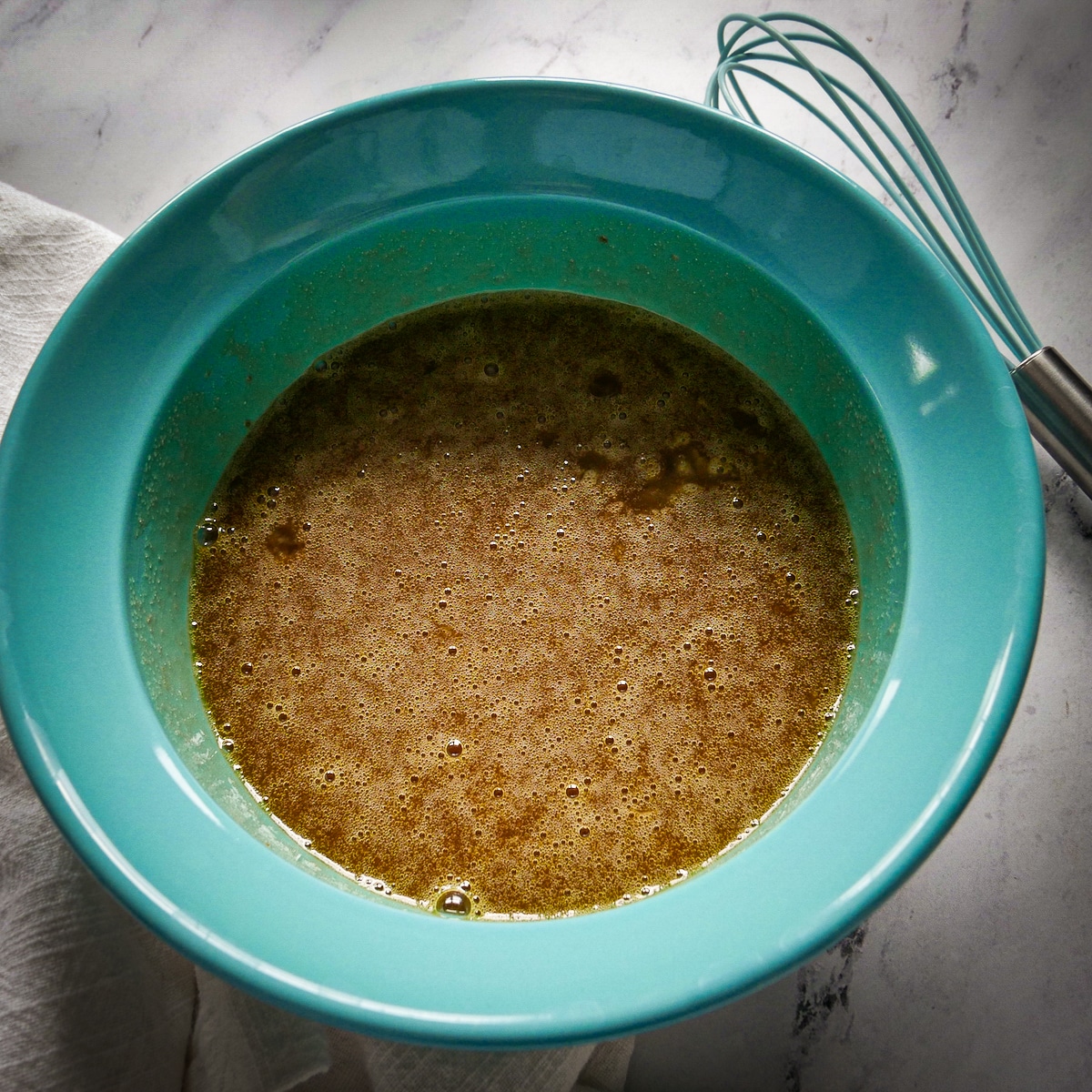 wet-ingredients-in-bowl.jpg Eggs, oil, brown sugar, and vanilla extract whisked together in a blue bowl.