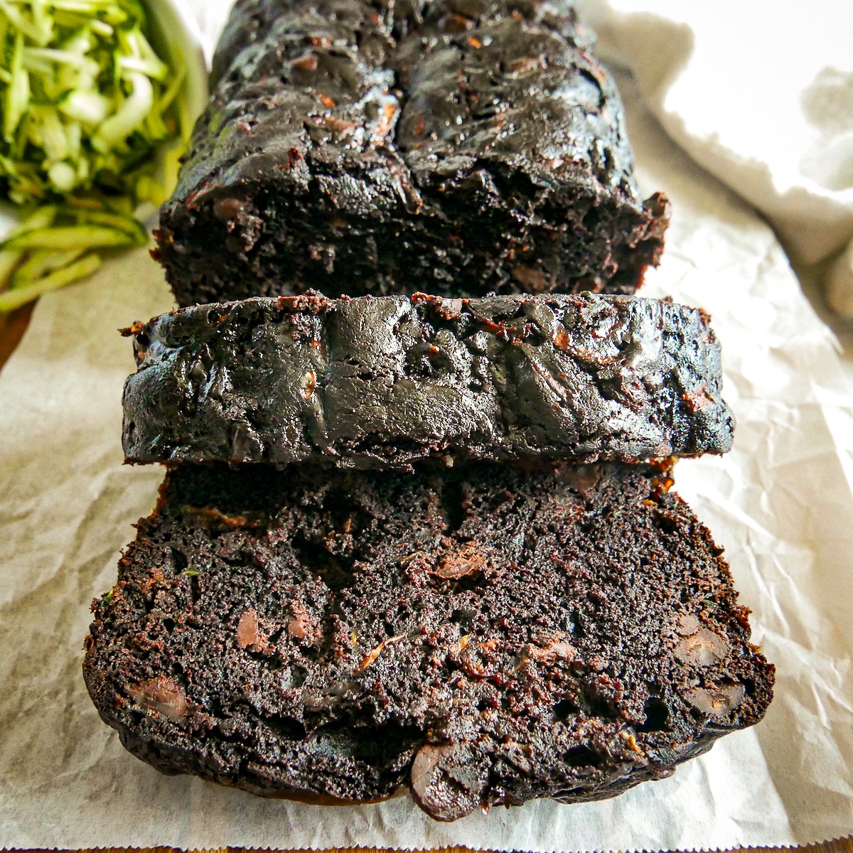 chocolate-zucchini-loaf.jpg chocolate zucchini loaf sliced on parchment paper.