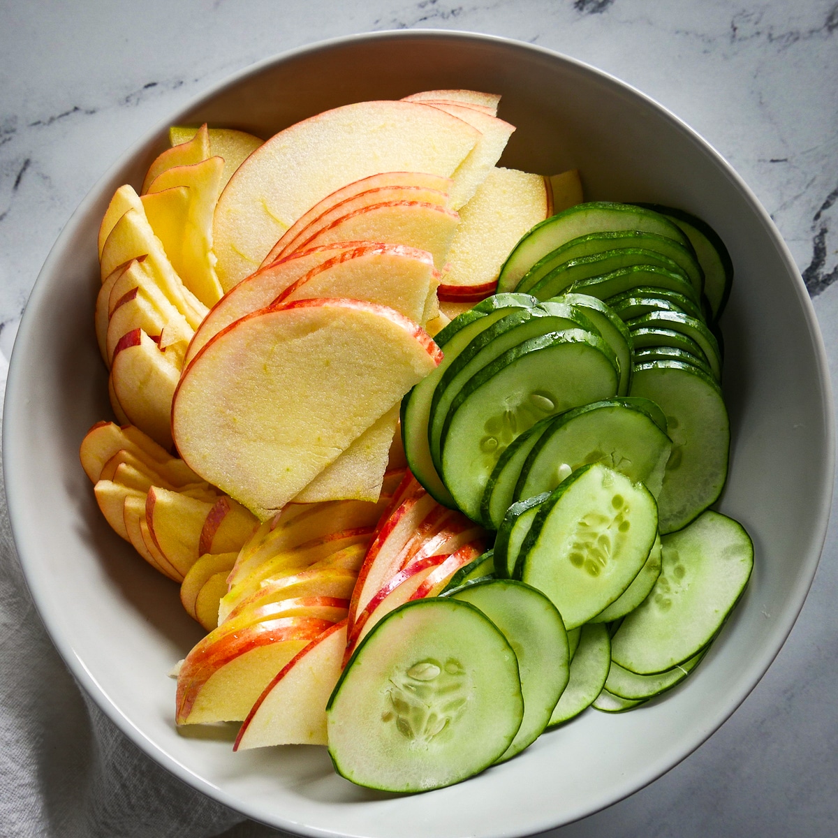 sliced-apples-and-cucumber.jpg thinly sliced apples and cucumber in a mixing bowl.