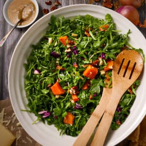 Roasted squash salad in a bowl with arugua, Parmesan cheese, and pecans.