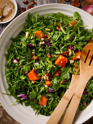 Roasted squash salad in a bowl with arugua, Parmesan cheese, and pecans.